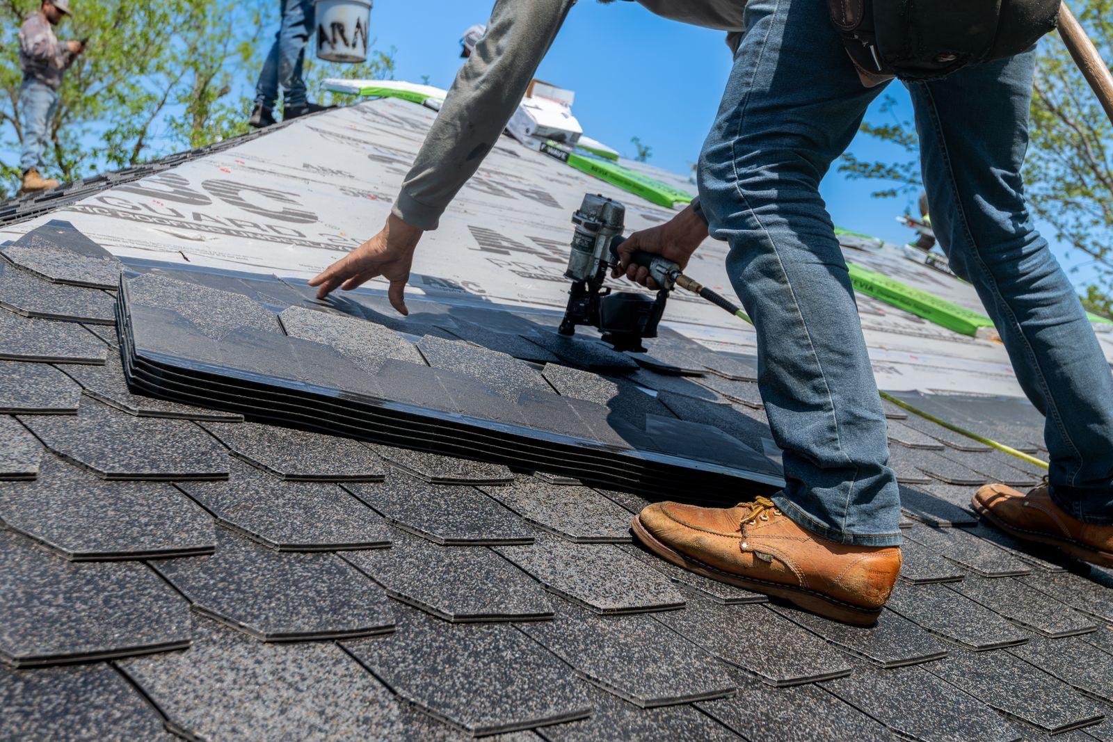 Roofer fixing asphalt shingles with a nail gun